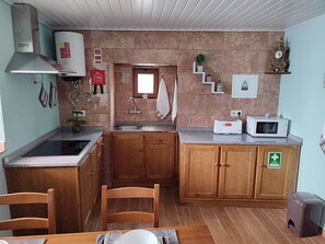 Una cucina compatta con mobili in legno, piano cottura integrato, forno a microonde e lavandino piccolo.