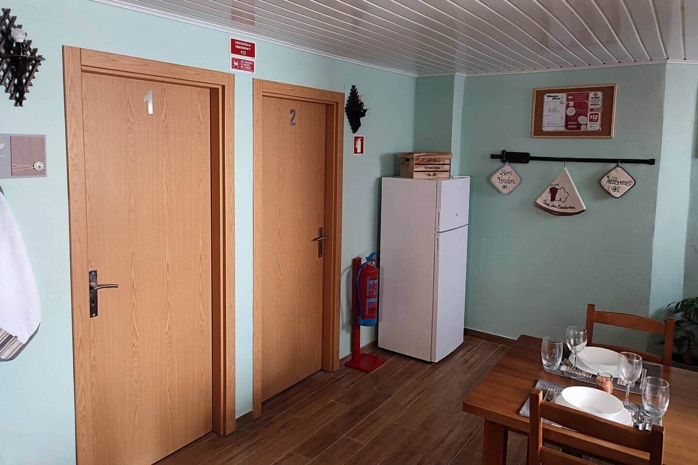 Ein Zimmer mit zwei Holztüren, einem weißen Kühlschrank, einem Esstisch mit Tellern und Gläsern sowie einem Feuerlöscher.
