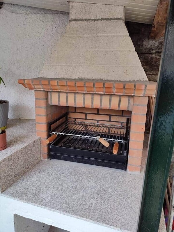 A brick-built outdoor grill with a chimney, a metal rack, and a wooden handle.