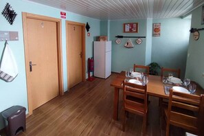 A dining area with wooden tables and chairs, a white refrigerator, and a fire extinguisher.