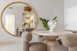 A dining area with a round table, cushioned chairs, a large mirror, and a decorative vase with green leaves. - Luxury 1-bedroom apartment with direct beach access (DUBAI)
