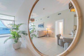 A modern living room with a large mirror reflecting the space, a sofa, a coffee table, and a dining area with chairs. - Luxury 1-bedroom apartment with direct beach access (DUBAI)