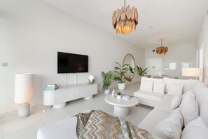 Een moderne woonkamer met een flatscreen televisie, een witte bank, een bijzettafeltje en een gebreid plaid.