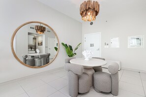Een moderne eetruimte met een ronde tafel, gestoffeerde grijze stoelen, een grote spiegel en een bijzondere houten hanglamp.