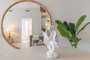 Een kamer met een ronde spiegel, een witte sculptuur en een groene plant op een tafel.