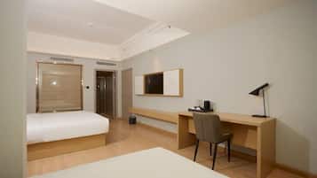 Habitación de hotel con cama, escritorio, silla, televisor e iluminación en el techo.