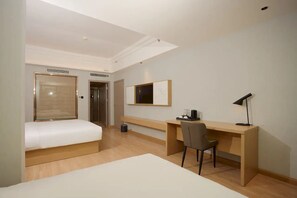 Habitación de hotel con cama, escritorio, silla, televisor e iluminación en el techo.