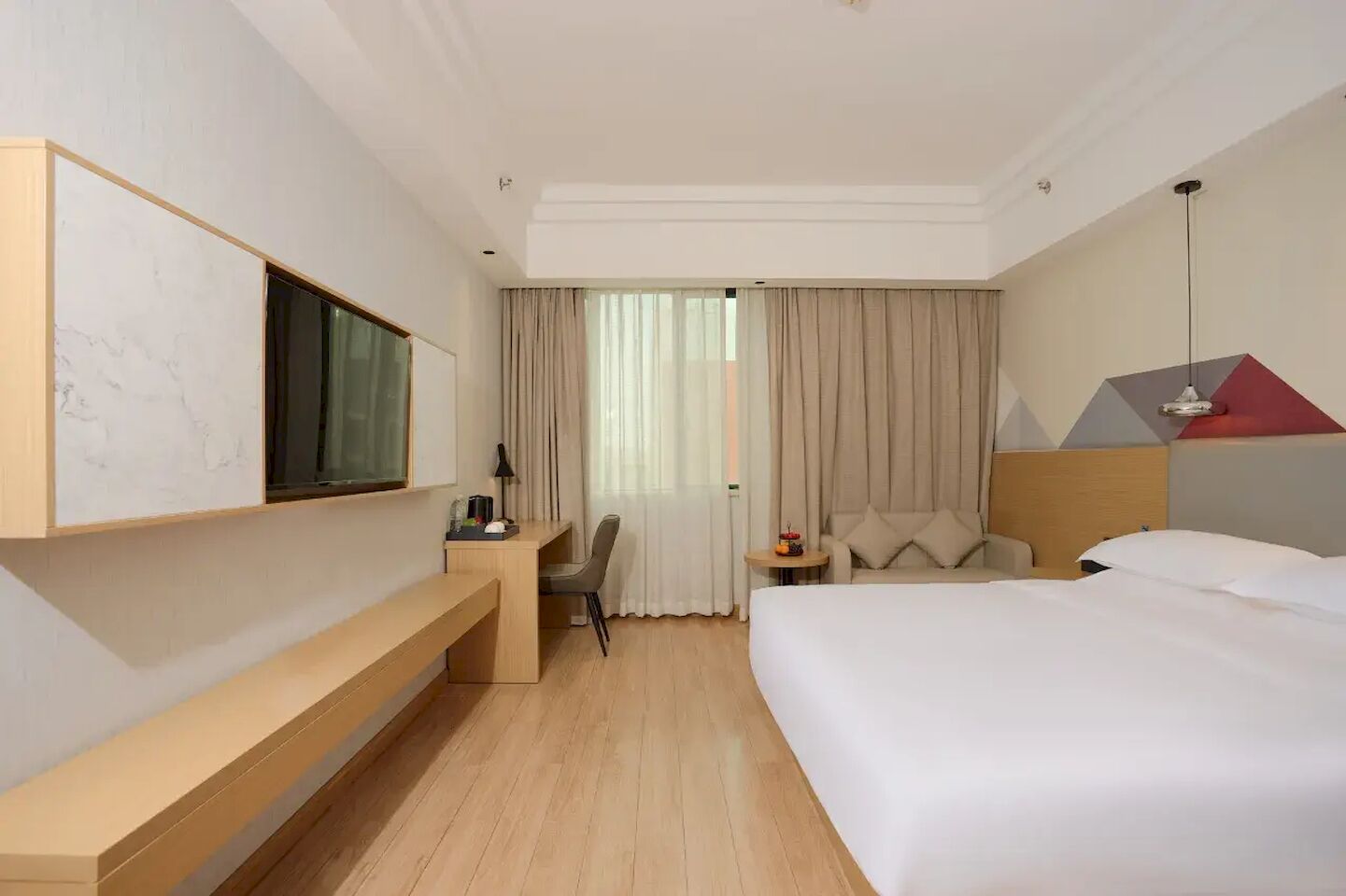 A hotel room with a bed, a desk, a chair, a TV, and a window with curtains.
