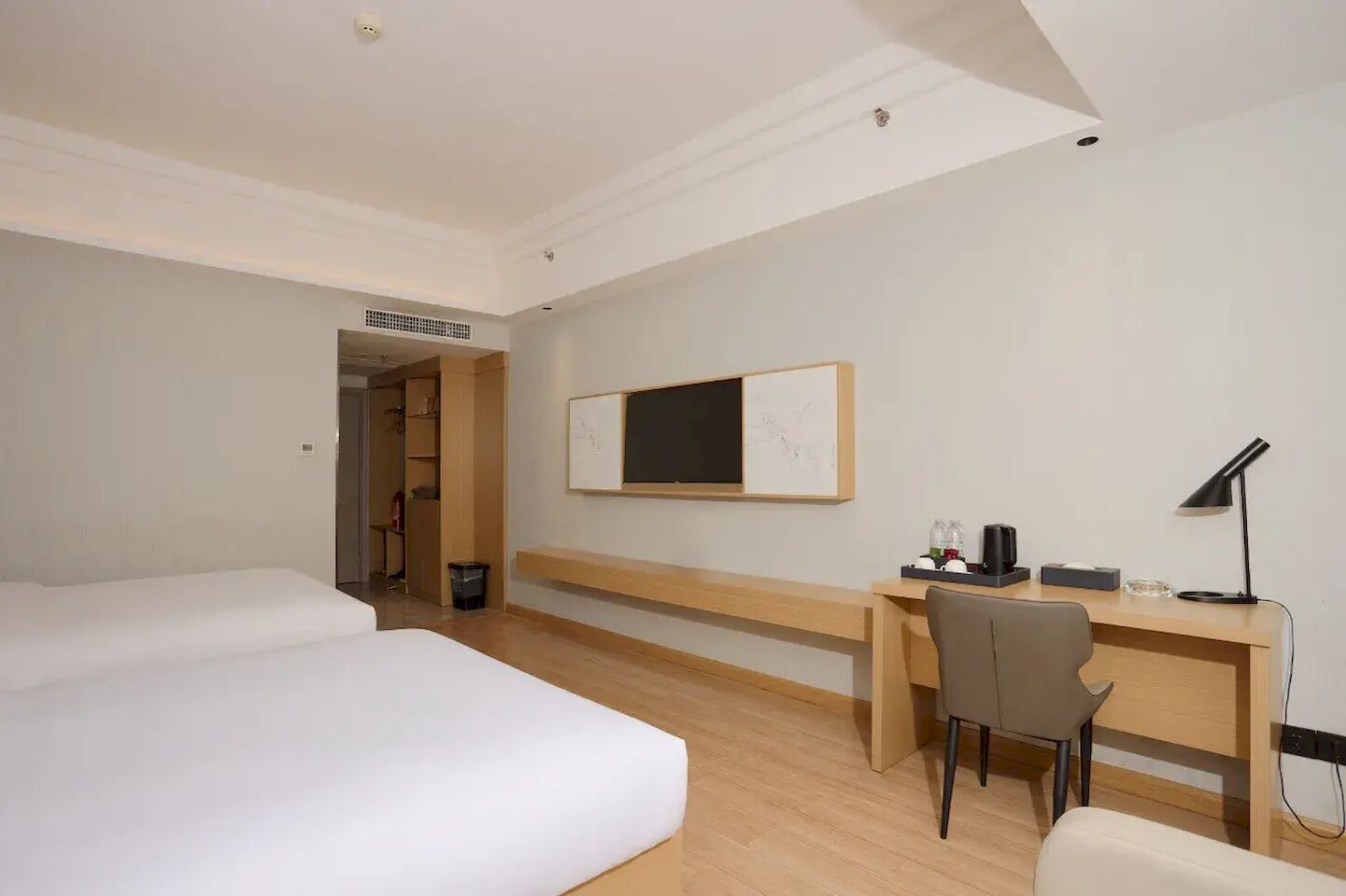 Habitación de hotel con dos camas, un escritorio, una silla, una lámpara de escritorio y televisión montada en la pared.