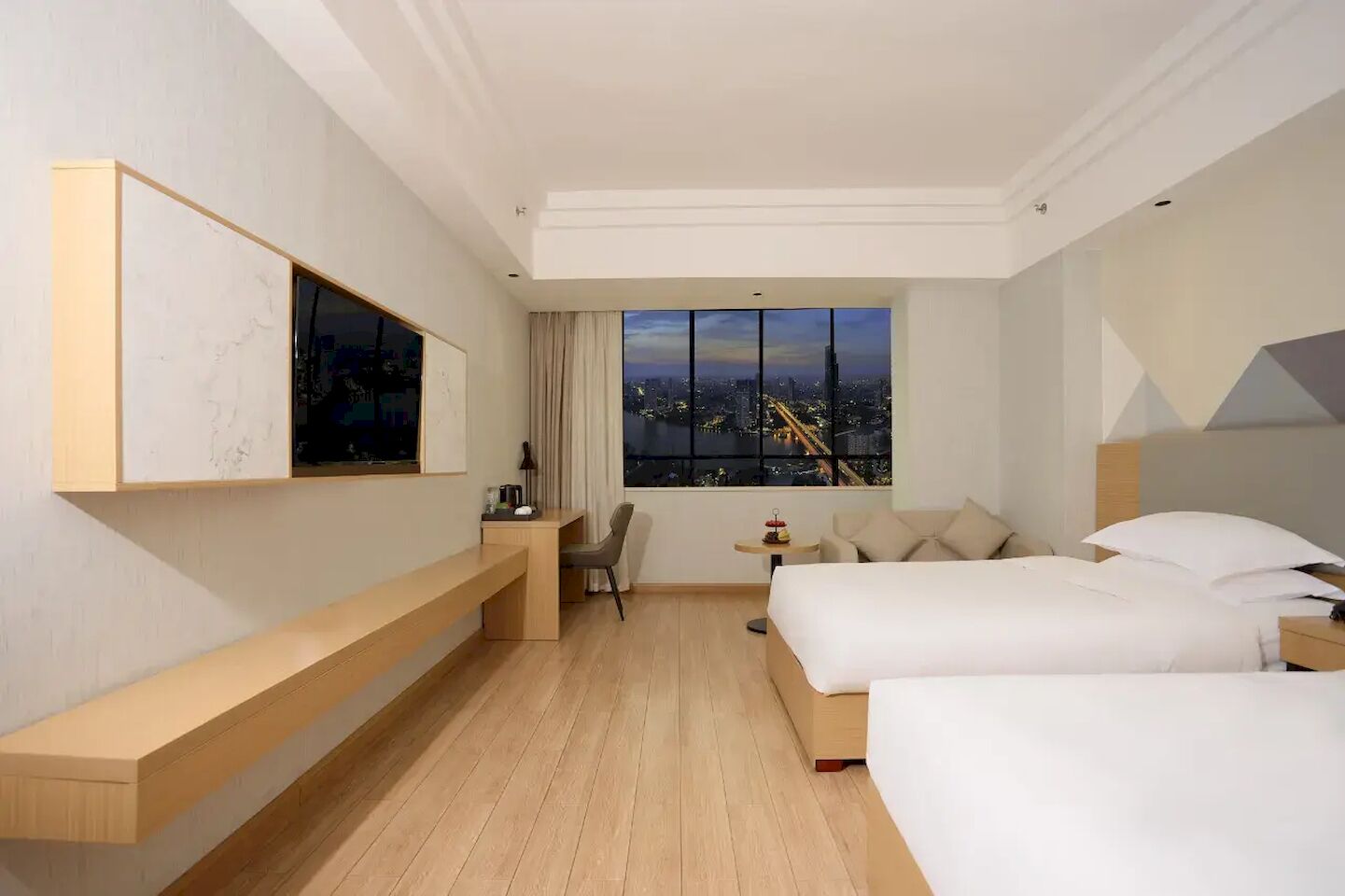 Una habitación de hotel con un ventanal grande, un escritorio, dos camas y una silla.