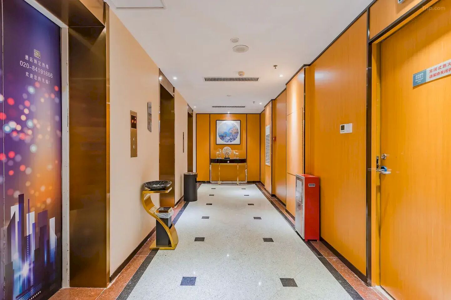 A hotel corridor with a tiled floor, a reception desk, a framed artwork on the wall, and a door with a sign.