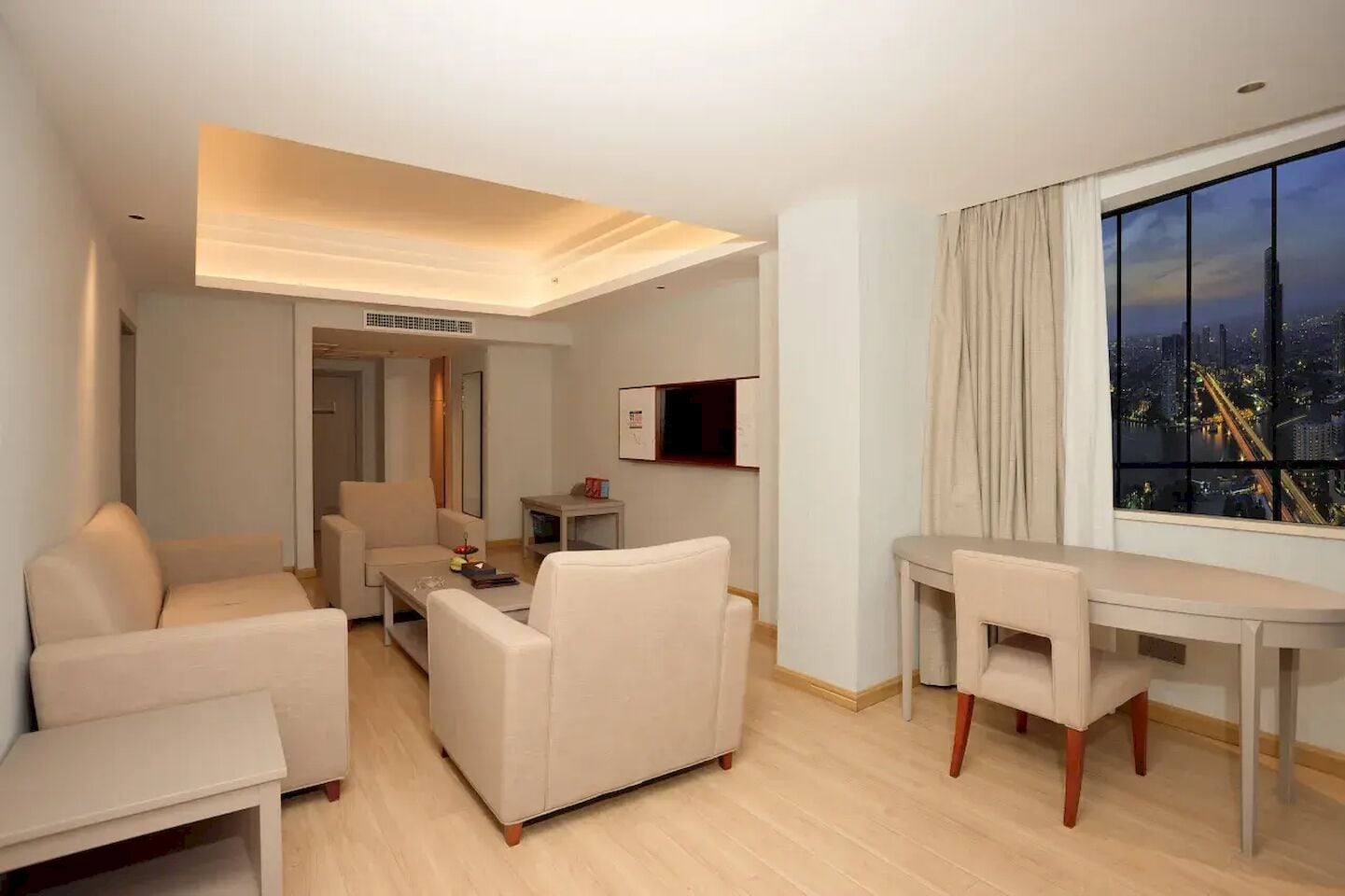 Habitación de hotel moderna con vistas a la ciudad, zona de comedor y sala de estar con sofá y mesa de centro.