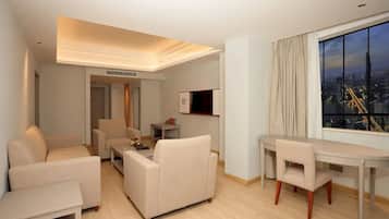 Habitación de hotel moderna con vistas a la ciudad, zona de comedor y sala de estar con sofá y mesa de centro.