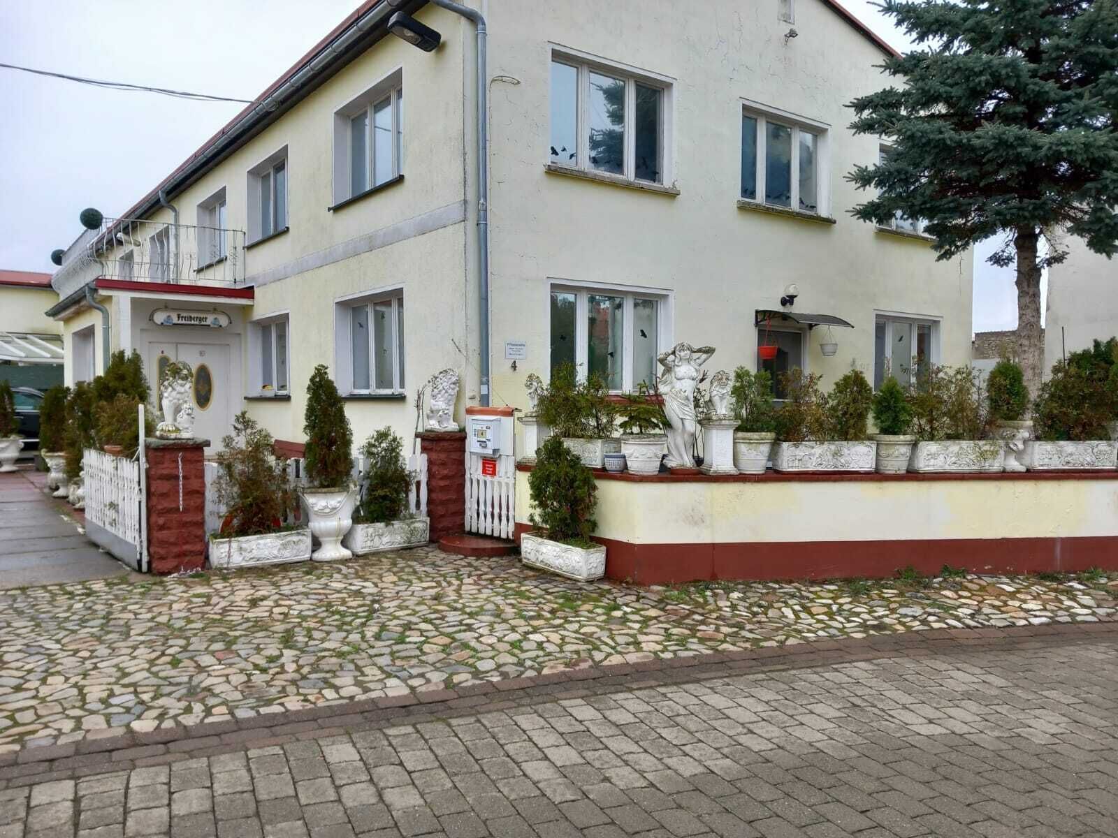 A two-story building with a tiled entrance and a small garden area with potted plants.