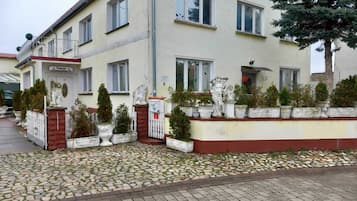 A two-story building with a tiled entrance and a small garden area with potted plants.