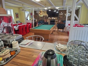 A pool table in a room with a brick fireplace, dining area with red chairs, and a television mounted on the wall. - Vrbo Property (Wanzleben-Börde)