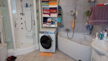 Ein Badezimmer mit Duschkabine, Waschmaschine, Badewanne und Ablagefläche mit gefalteten Handtüchern.