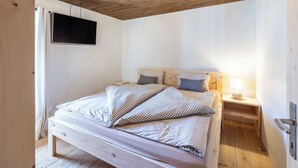 A bedroom with a wooden ceiling, a bed with checkered bedding, a flat-screen TV, and a bedside lamp.