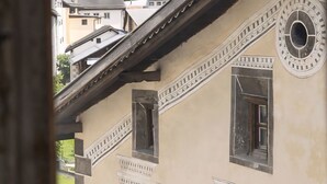 A building with a traditional architectural style, featuring a balcony and a view of snow-capped mountains in the background.