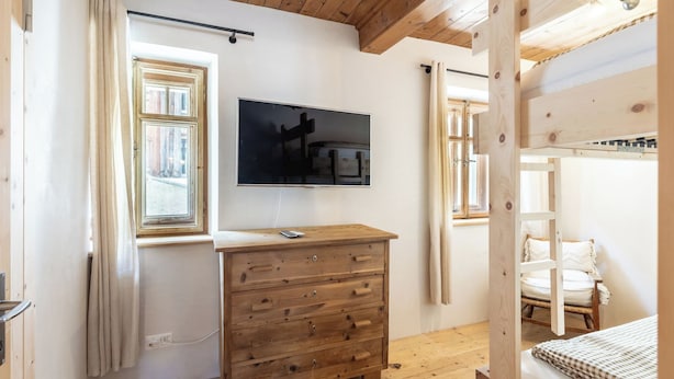 A room with a wooden dresser, a television mounted on the wall, and a window with curtains.