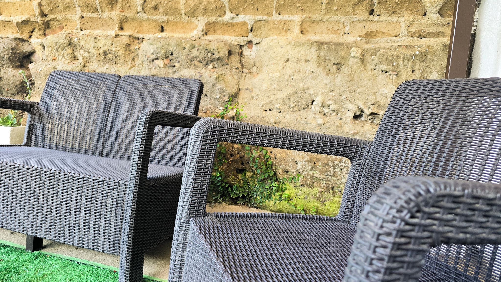 Korbmöbel im Freien vor einer Steinwand.