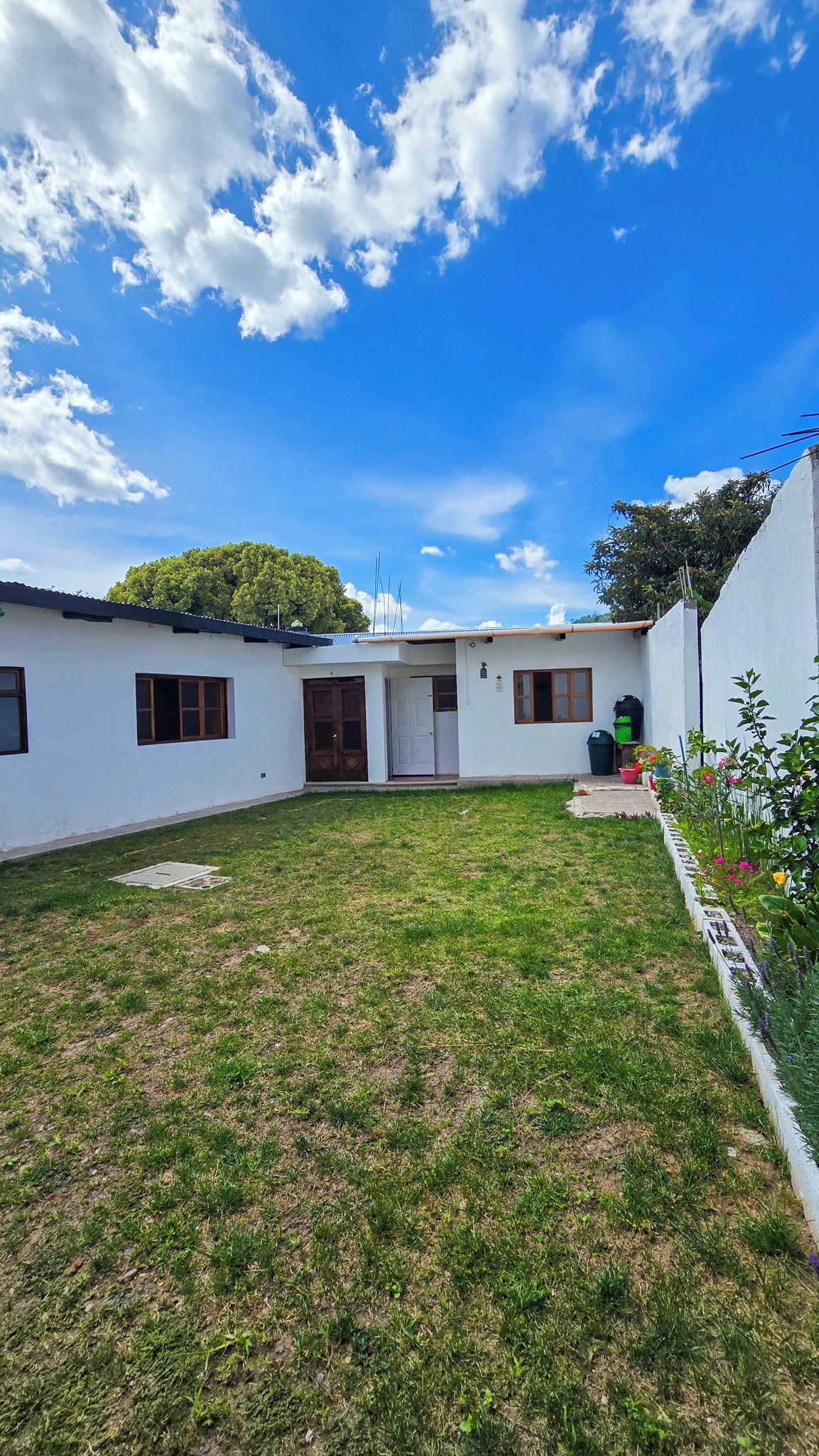 Um imóvel residencial com fachada branca, porta de entrada, pequeno jardim frontal e céu azul com nuvens.