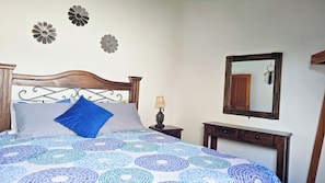A bedroom with a bed, a nightstand, a lamp, a mirror, and wall decorations. - Feel at home in Antigua, just 7 min from La Merced, for up to 12 guests (La Antigua Guatemala)