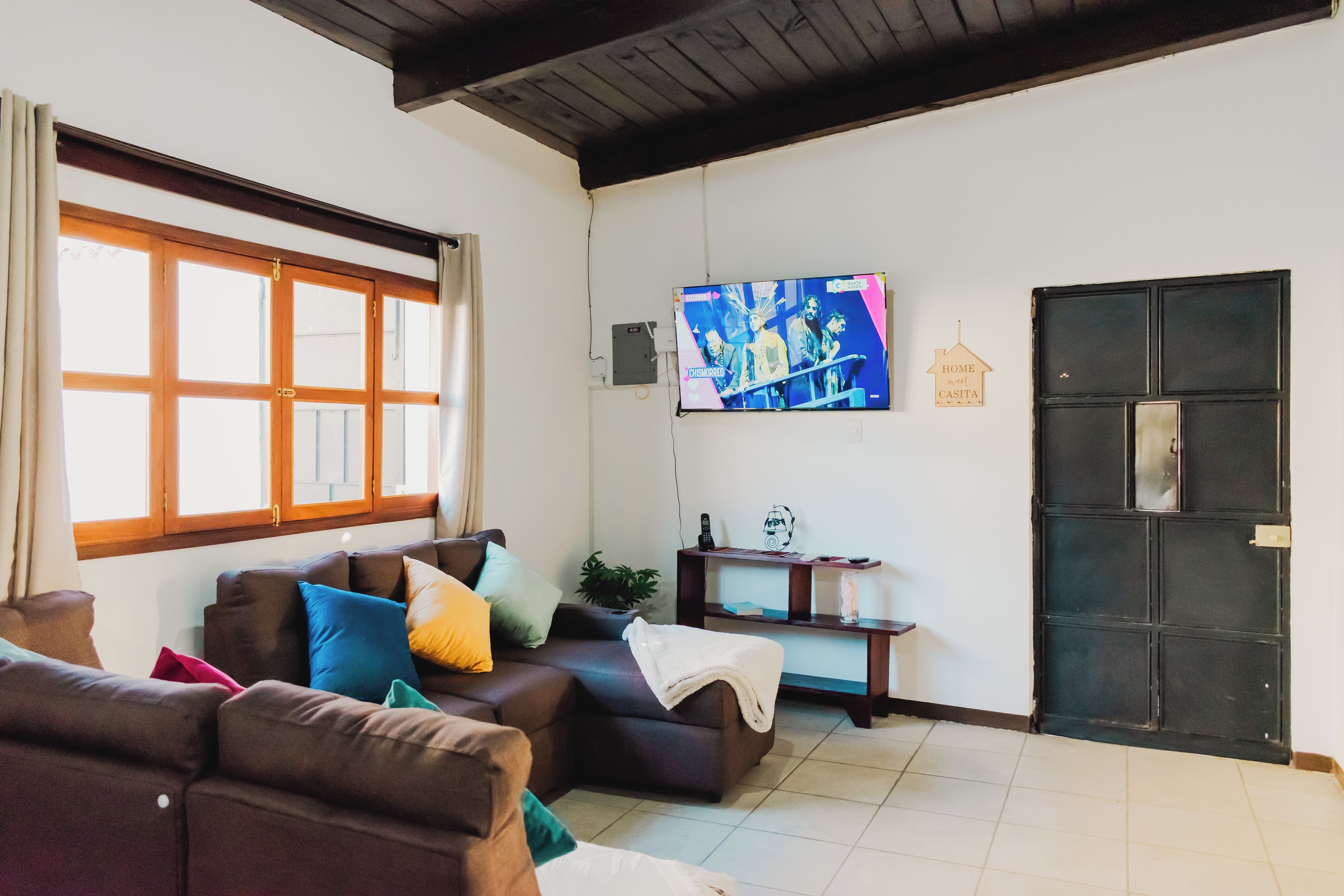 Uma sala de estar com sofá, televisão na parede e uma porta.