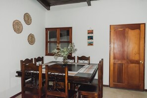 A dining area with a wooden table and chairs, a vase with flowers, and wall decorations including framed pictures and a wooden door. - Feel at home in Antigua, just 7 min from La Merced, for up to 12 guests (La Antigua Guatemala)