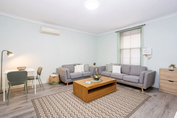 A modern living room with a sofa set, a coffee table, a lamp, and a window with blinds. - Heart of Freo - Charming Heritage Stay (Fremantle)