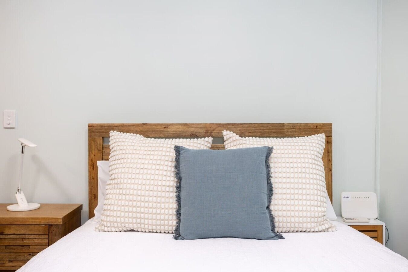 A bed with a wooden headboard, two white textured pillows, and a blue pillow.