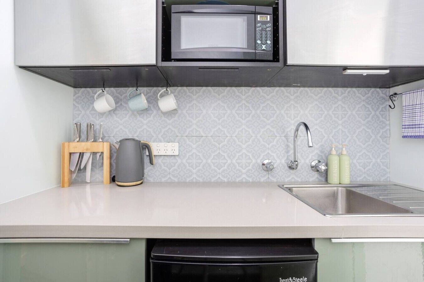 A modern kitchen with a microwave, kettle, sink, and utensils.