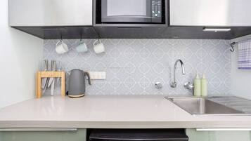 A modern kitchen with a microwave, kettle, sink, and utensils.