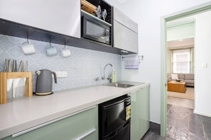 A modern kitchen with a built-in dishwasher, a kettle, and a microwave. - Heart of Freo - Charming Heritage Stay (Fremantle)