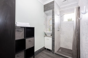 A modern bathroom with a shower, a sink, and a mirror. There is a dark-colored wardrobe with multiple compartments. - Heart of Freo - Charming Heritage Stay (Fremantle)