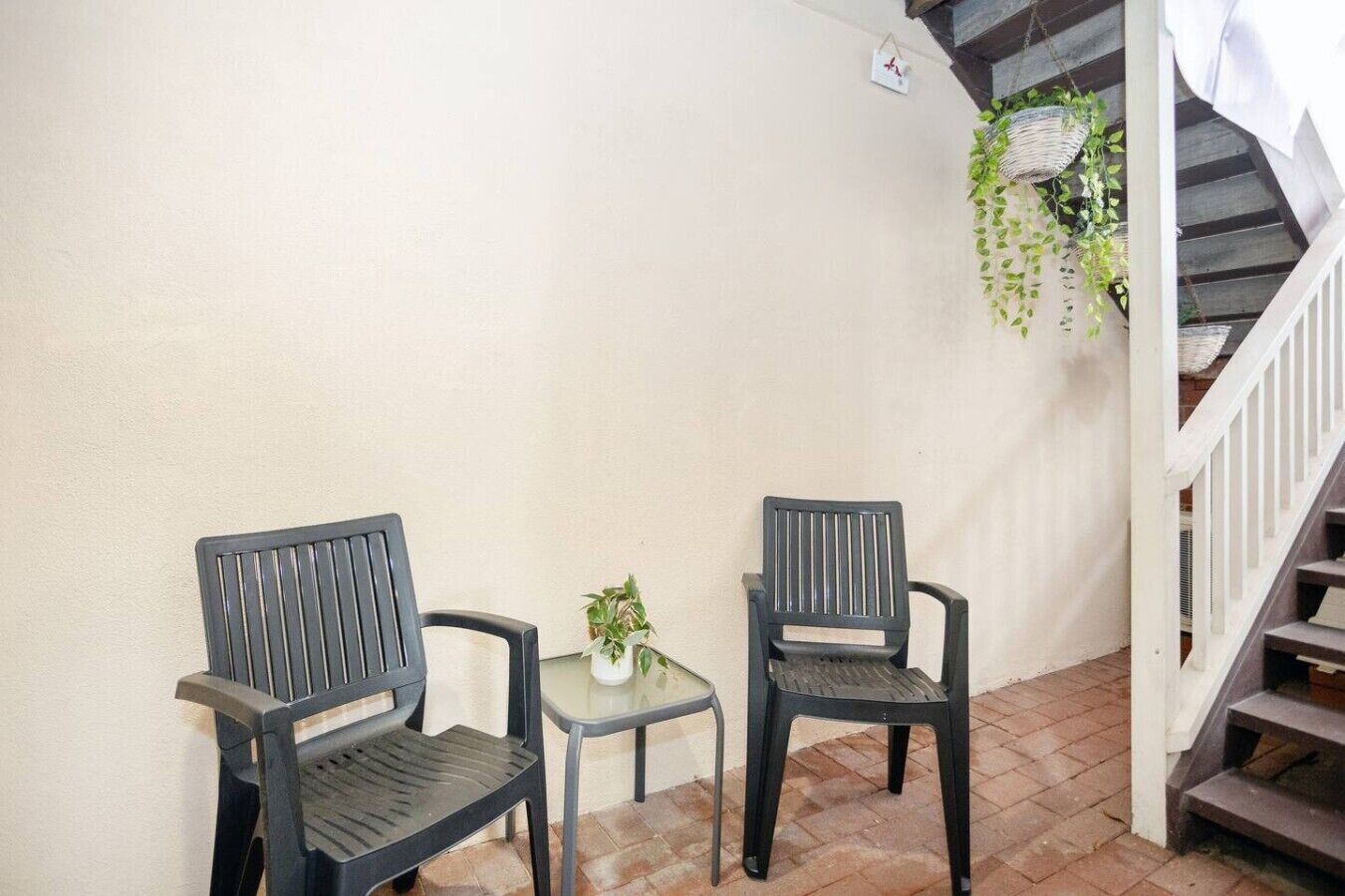 A small outdoor seating area with two chairs and a table, a potted plant, and a staircase.