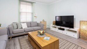 A modern living room with a grey sofa, a wooden coffee table, a flat-screen TV on a white stand, and a patterned rug. - Heart of Freo - Charming Heritage Stay (Fremantle)
