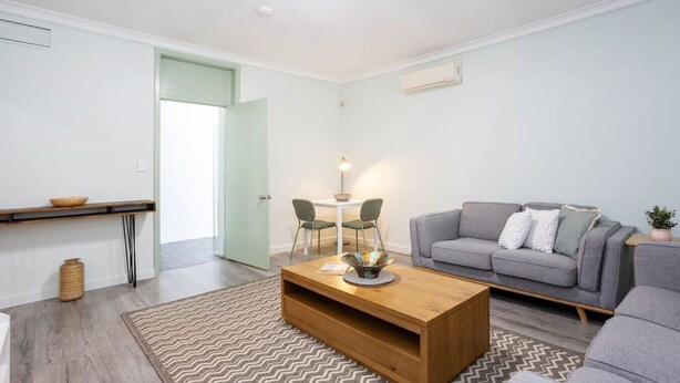 A modern living room with a grey sofa, a wooden coffee table, and a dining area with a table and chairs. - Heart of Freo - Charming Heritage Stay (Fremantle)