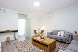 A modern living room with a grey sofa, a wooden coffee table, and a dining area with a table and chairs. - Heart of Freo - Charming Heritage Stay (Fremantle)