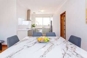A modern kitchen with a marble dining table, chairs, and a fruit bowl. - Sandcastle Loft - The Ultimate Fremantle Escape (Fremantle)