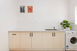 A kitchen with a washing machine, a sink, and two decorative items on the wall. - Sandcastle Loft - The Ultimate Fremantle Escape (Fremantle)