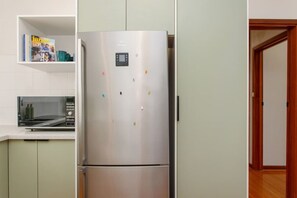 A kitchen with a stainless steel refrigerator, a microwave, and a shelf with books. - Sandcastle Loft - The Ultimate Fremantle Escape (Fremantle)