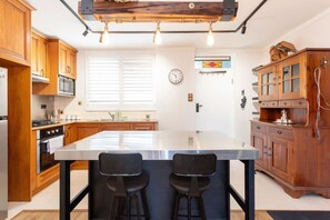 A kitchen with wooden cabinets, a large island with bar stools, a microwave, and a clock on the wall. - The Lab - Heart of North Fremantle (North Fremantle)