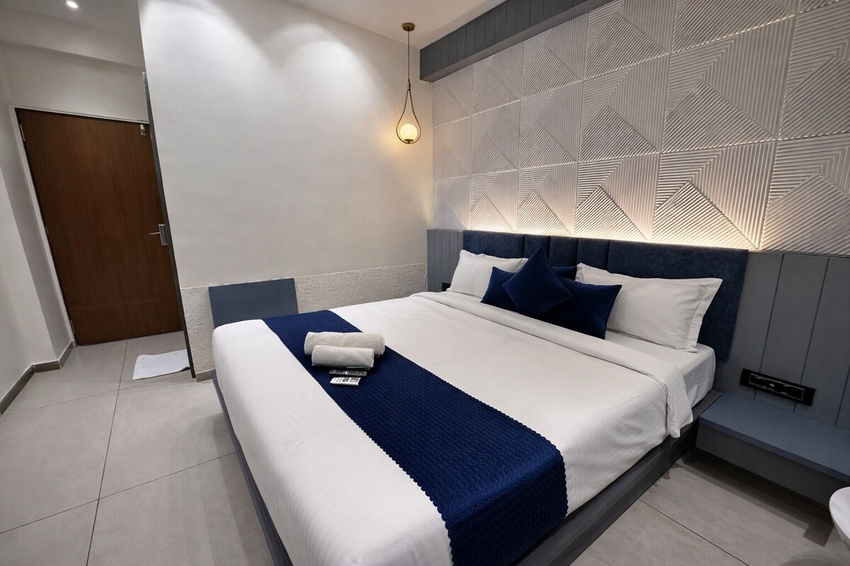 Una habitación de hotel moderna con una cama grande, cabecera con diseños geométricos y una mesita de noche con lámpara.