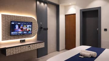Habitación de hotel con televisor montado en una pared texturizada, cama con detalles en azul y puerta de madera.