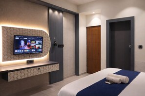 A hotel room with a TV mounted on a textured wall, a bed with a blue accent, and a wooden door.
