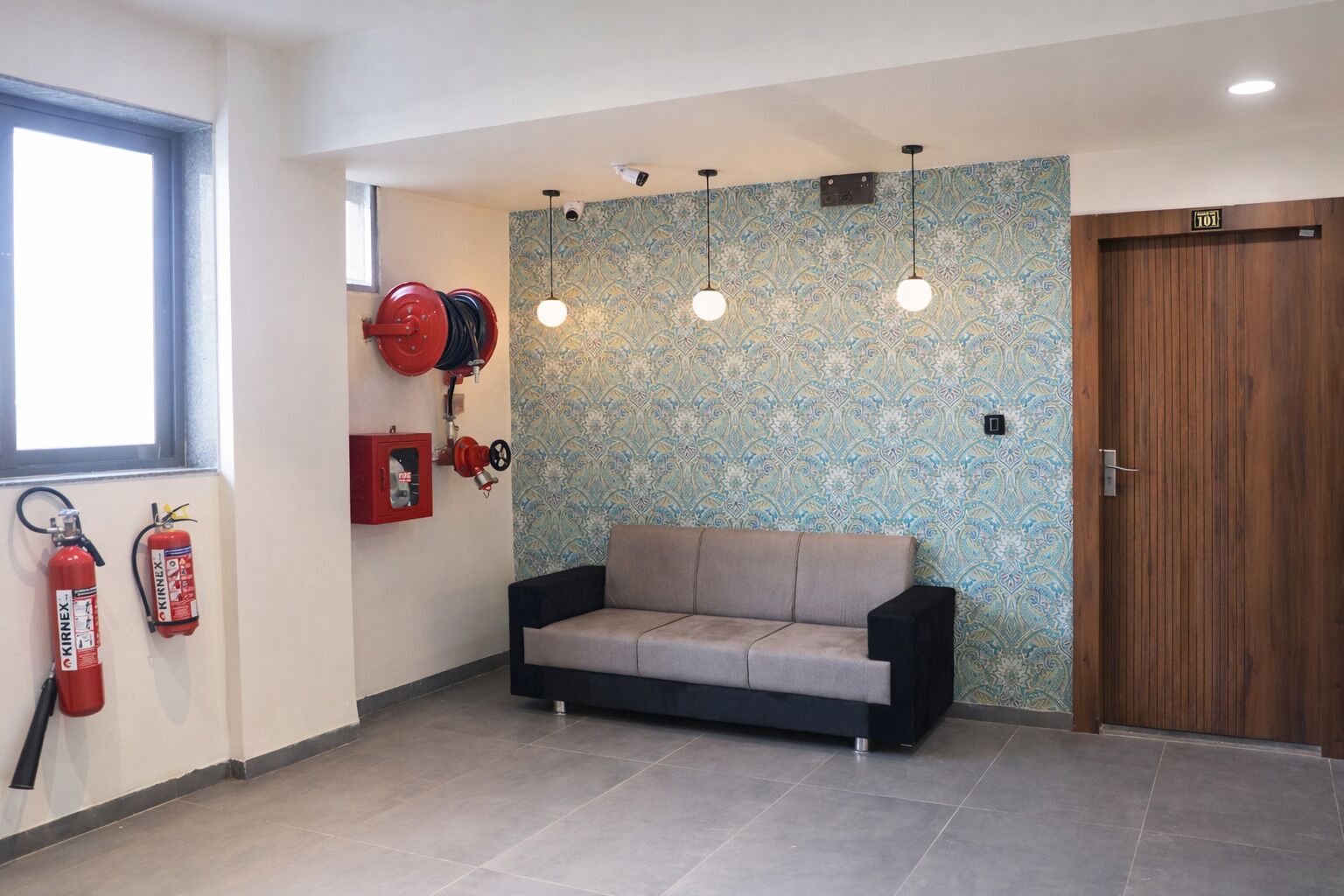A room with a sofa, fire extinguishers, a wooden door, and patterned wallpaper.