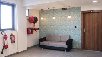 A room with a sofa, fire extinguishers, a wooden door, and patterned wallpaper.