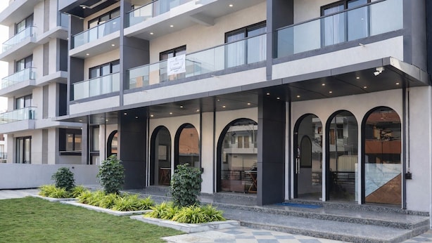 A multi-story hotel with a modern design, featuring balconies, large windows, and a checkered pavement area. - Axon Business Hotel Sanand Ahmedabad (Ahmedabad)