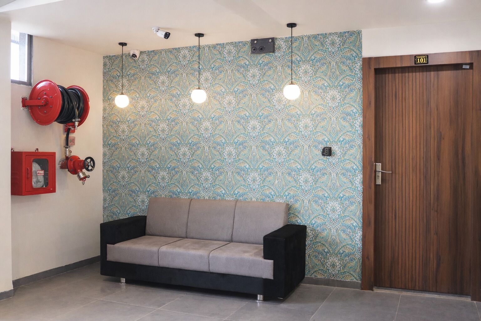 Ein Zimmer mit Wandverkleidung, einer Couch, einer Tür mit der Aufschrift '101' und einem Feuerlöscher.